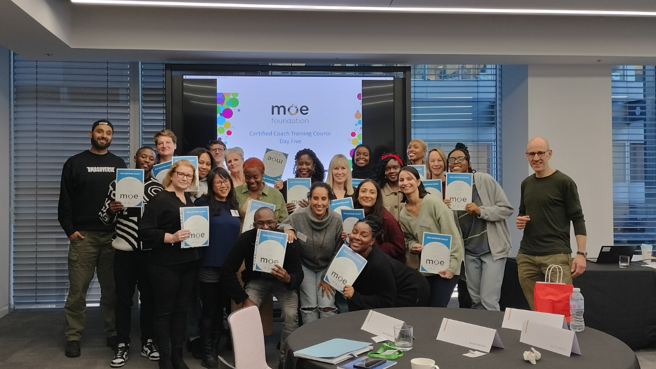 A group photo of people holding their Coach Certification certificates on graduation day in an office